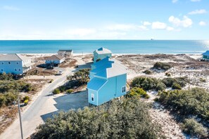 Una propiedad costera con una casa azul destacada, un camino de tierra y una playa al fondo.