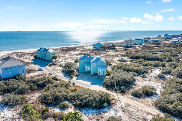 Una zona costera con varias casas, algunas con techos azules, rodeada de vegetación y una playa.