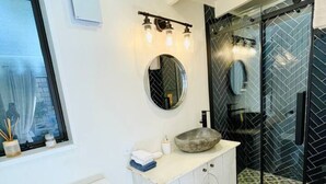 Un baño moderno con inodoro blanco, un espejo redondo y un tocador con un salpicadero de diseño en espiga.