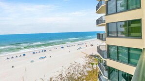 A beach view from a hotel balcony with a sandy beach, umbrellas, and ocean.