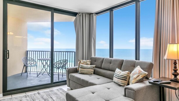 A balcony with a sofa and chairs, a view of the ocean, and a lamp on a side table.