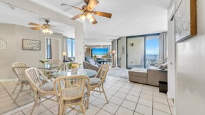 A spacious living area with a glass dining table, wicker chairs, a sofa, and a ceiling fan.