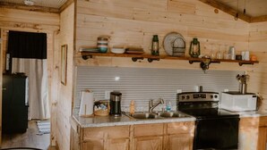 A rustic kitchen with wooden walls, a ceiling fan, and basic appliances. - Cozy tiny cabin, close to local activities. Pet friendly. Suited 2 adults. (Owenton)