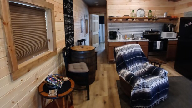 A cozy cabin interior with a dining area, a kitchen, and a seating area with a blanket. - Cozy tiny cabin, close to local activities. Pet friendly. Suited 2 adults. (Owenton)