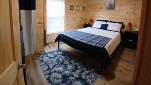 A wooden-paneled room with a bed, a nightstand, a window with blinds, and a ceiling light. - Cozy tiny cabin, close to local activities. Pet friendly. Suited 2 adults. (Owenton)
