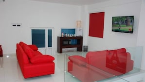 Un salon moderne avec un canapé rouge, une table basse en verre, un téléviseur fixé au mur et un distributeur d’eau.