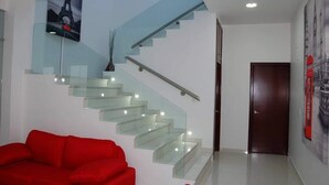 Un intérieur moderne avec un escalier en verre, un canapé rouge et une porte ornée d’une affiche.