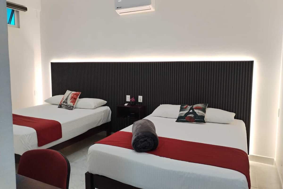 A hotel room with two beds, a desk, and a chair. There is a wall-mounted air conditioner above the beds.