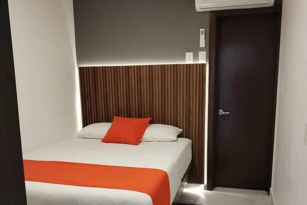 A hotel room with a bed, a wooden headboard, an air conditioning unit, and a door.