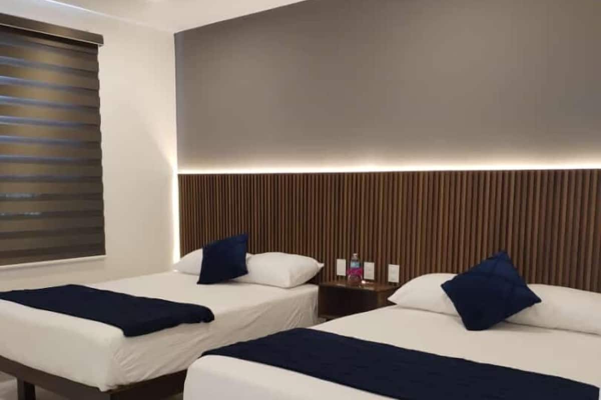 A hotel room with two beds, each with a dark blue bedspread and pillows, a wooden headboard, and a window with blinds.