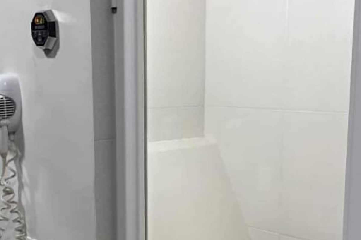 A bathroom with a white tiled wall, a black tiled shower area, a white sink with a faucet, and a towel rack.