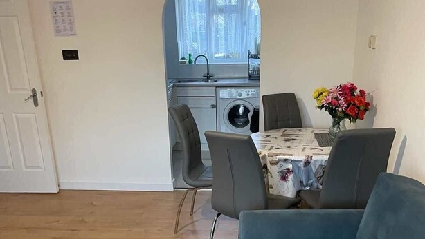 A living room with a blue sofa, a glass coffee table, and a dining area with a table and chairs. - Charming Escape: 2BR Home with Parking (Aveley)