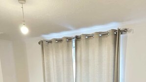 A single bed with a headboard, a bedside table, and a window with curtains. - Charming Escape: 2BR Home with Parking (Aveley)
