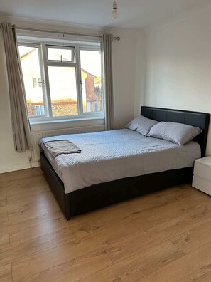 A bedroom with a bed, a window, and a white nightstand. - Charming Escape: 2BR Home with Parking (Aveley)