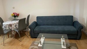 A living room with a dark blue sofa, a glass coffee table, and a dining table with chairs. - Charming Escape: 2BR Home with Parking (Aveley)