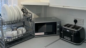A kitchen with a dish rack, microwave, toaster, and white cabinets. - Charming Escape: 2BR Home with Parking (Aveley)