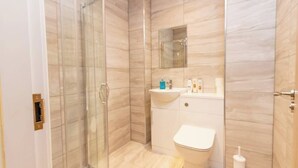 Casa de banho com cabine de duche em vidro, lavatório branco e sanita.