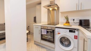 Uma cozinha compacta com forno embutido, micro-ondas e máquina de lavar roupa, e um pequeno espaço de estar com um sofá.