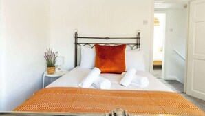 Quarto de hotel com uma cama, uma mesinha de cabeceira, um travesseiro vermelho e um edredom estampado.