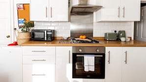Uma cozinha moderna com armários brancos, exaustor de aço inoxidável, micro-ondas, torradeira e forno.