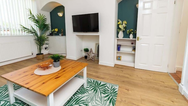 Uma sala de estar com uma mesa de madeira, uma televisão de tela plana, uma estante e uma porta.