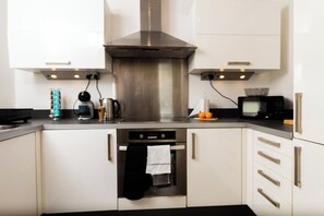 Una cocina moderna con electrodomésticos de acero inoxidable, armarios blancos y un horno empotrado.