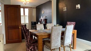 A dining area with a wooden table and chairs, a clock on the wall, and a door leading to another room. - Beautifully Styled 2BR Home with Garden (Manchester)