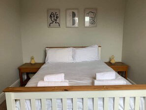 Una cama bien hecha con ropa blanca, dos mesitas de noche con lámparas y tres cuadros en la pared.
