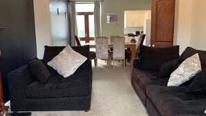 A living room with two sofas, a dining table, chairs, and a kitchen area in the background. - Beautifully Styled 2BR Home with Garden (Manchester)