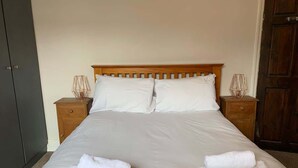 A bed with white linens, two bedside tables with lamps, and a wooden headboard. - Beautifully Styled 2BR Home with Garden (Manchester)