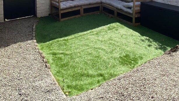 A residential property with a brick house, a black door with a heart symbol, a wooden bench, and a green artificial lawn. - Beautifully Styled 2BR Home with Garden (Manchester)