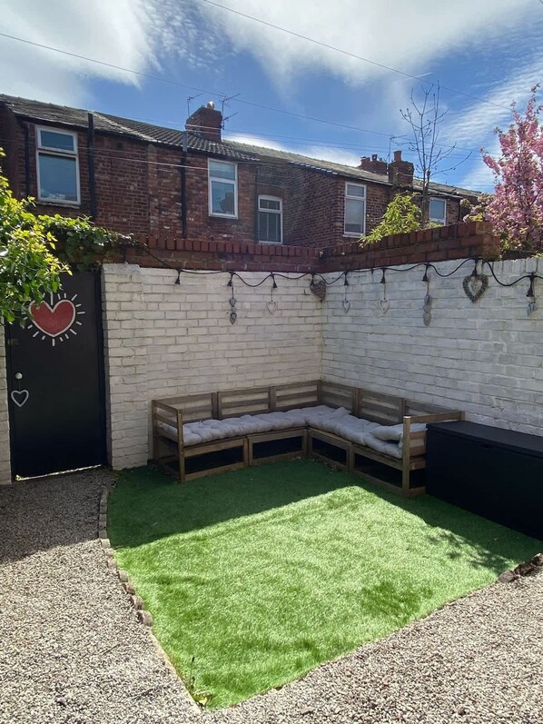 A residential property with a brick house, a black door with a heart symbol, a wooden bench, and a green artificial lawn.