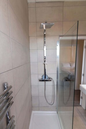 Une douche dotĂ©e dâune porte en verre, dâun pommeau de douche Ă main et dâun panneau de commande fixĂ© au mur.