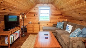 A cozy attic room with wooden walls, a television, a sofa, and a coffee table. - Windy Dreams: an idyllic, cozy seaside PEI cottage (Kensington)