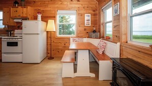 A cabin-style kitchen with wooden walls, a white refrigerator, stove, and a wooden table with benches. - Windy Dreams: an idyllic, cozy seaside PEI cottage (Kensington)