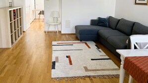 Een moderne woonkamer met een grijze bank, een witte bijzettafel, een kamerbreed tapijt met dessin en een boekenkast.