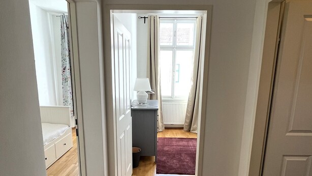 Een gang met houten vloer die leidt naar een slaapkamer met een bed en bureau.