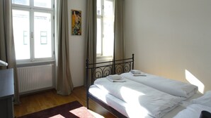 Een slaapkamer met een bed, een radiator, een raam met gordijnen en een schilderij aan de muur.