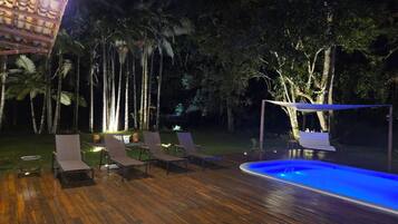 Un terrazzo in legno con poltrone relax e piscina di notte.