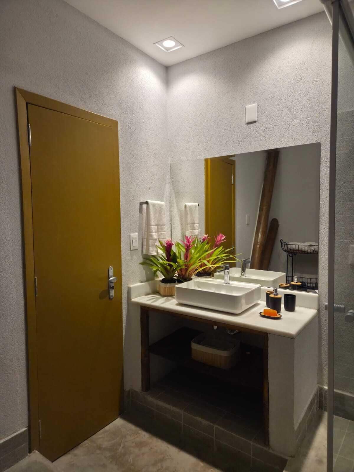 A modern bathroom with a large mirror, a sink, and a toilet. There is a plant on the sink and a towel hanging on the wall.