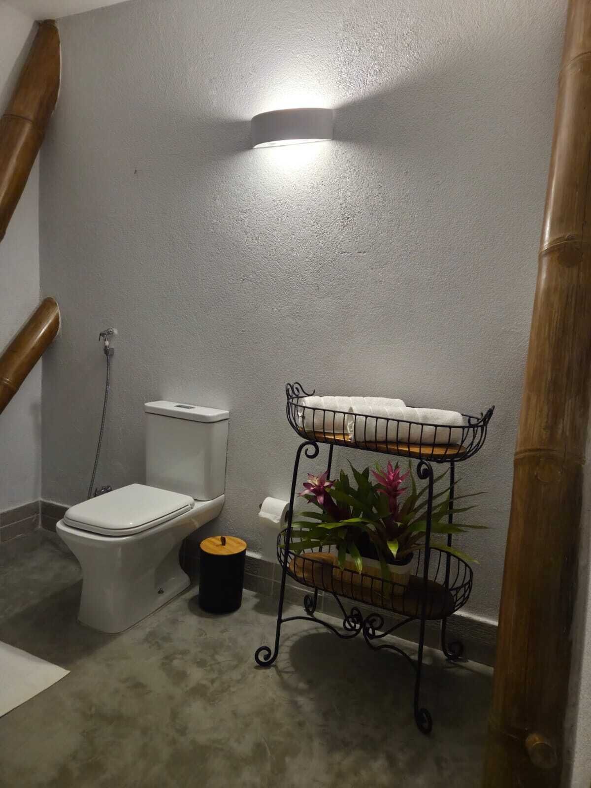 A bathroom with a toilet, a bidet, a small trash bin, and a metal shelf with plants.