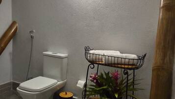 A bathroom with a toilet, a bidet, a small trash bin, and a metal shelf with plants.