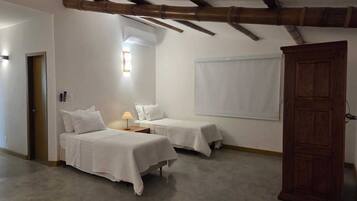 A room with two beds, a wooden door, and a window with blinds.