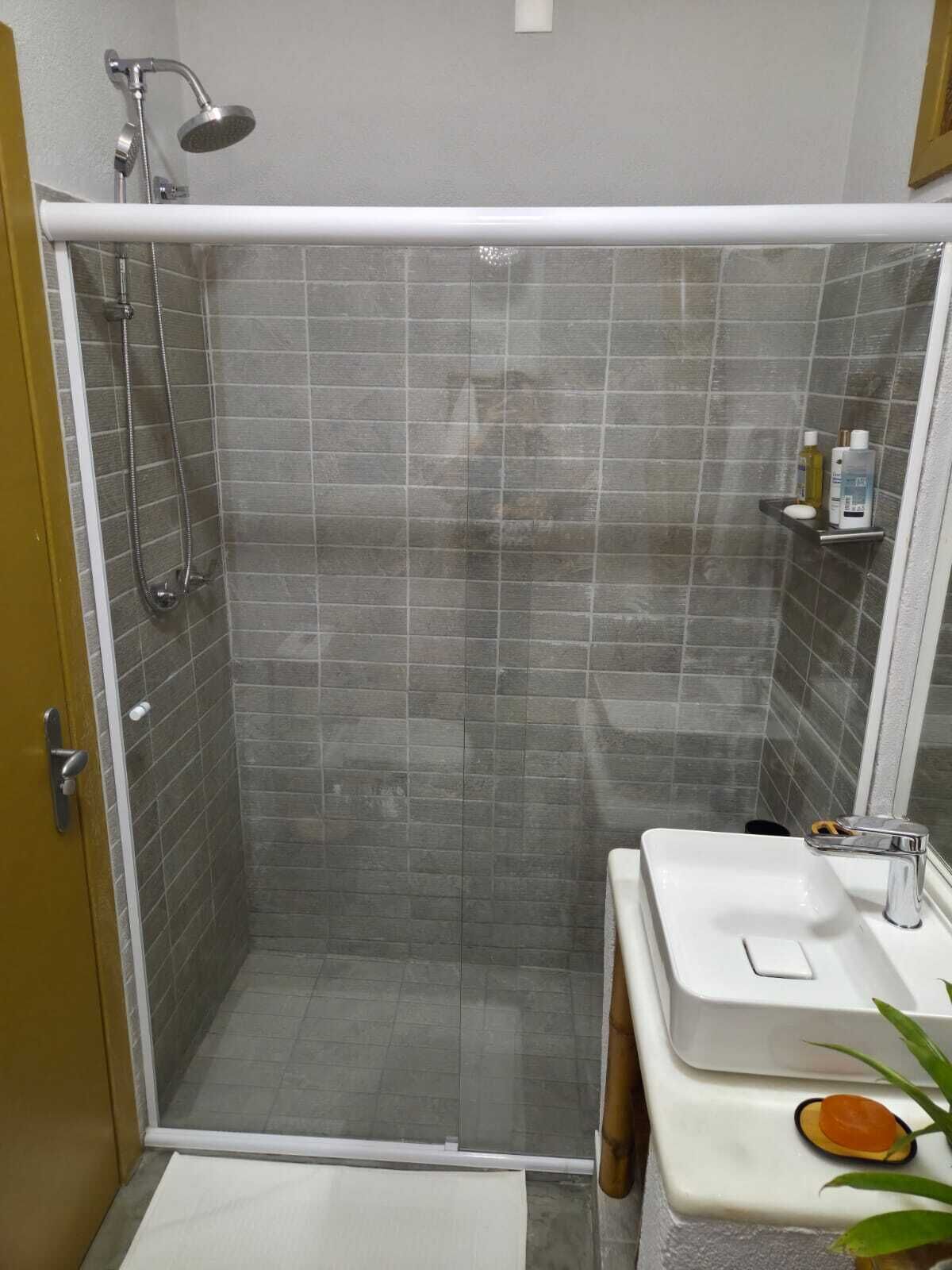 A shower with a handheld showerhead and a wall-mounted faucet, a white sink with a soap dispenser, and a small shelf with toiletries.