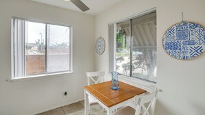 Una stanza con un tavolo in legno, sedie bianche, una ventola a soffitto e due finestre con tende.