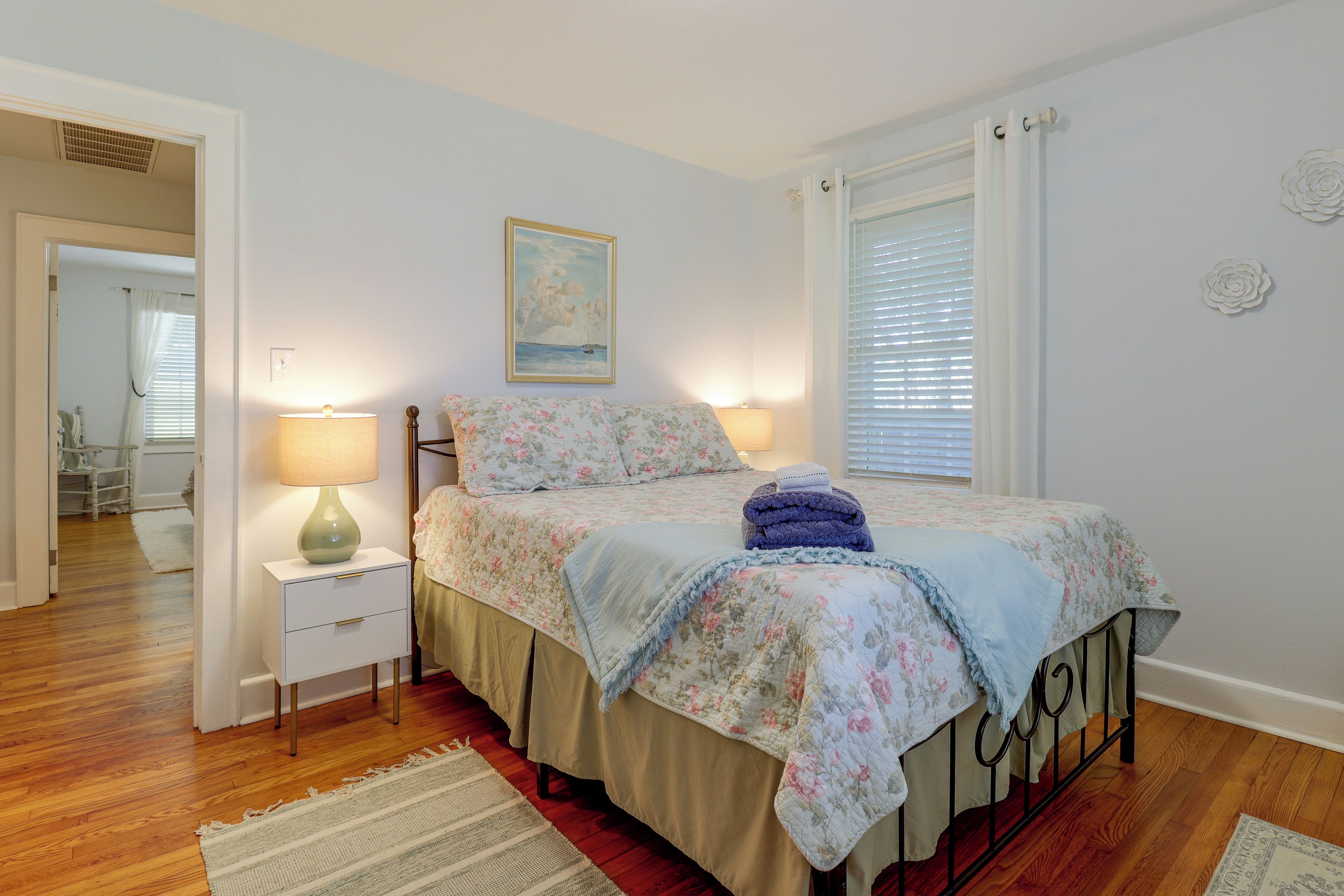 Une chambre à coucher avec un lit, des tables de chevet, une lampe, un tableau et une fenêtre avec des stores.