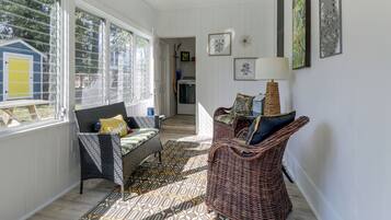 Een zonnige kamer met een rieten stoel, een gestoffeerde bank en een kamerbreed tapijt.