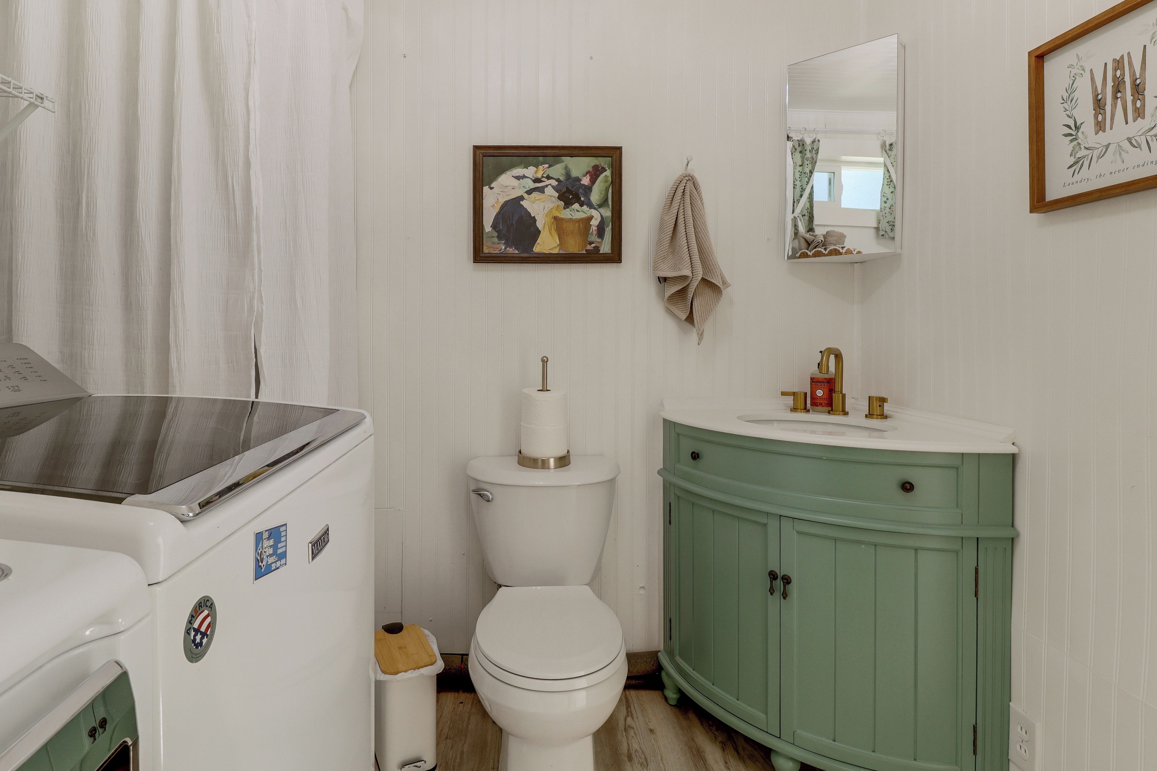 Une salle de bain avec des toilettes blanches, un meuble-lavabo vert, un tableau encadré au mur et une serviette suspendue à un crochet.