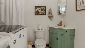 Une salle de bain avec des toilettes blanches, un meuble-lavabo vert, un tableau encadré au mur et une serviette suspendue à un crochet.