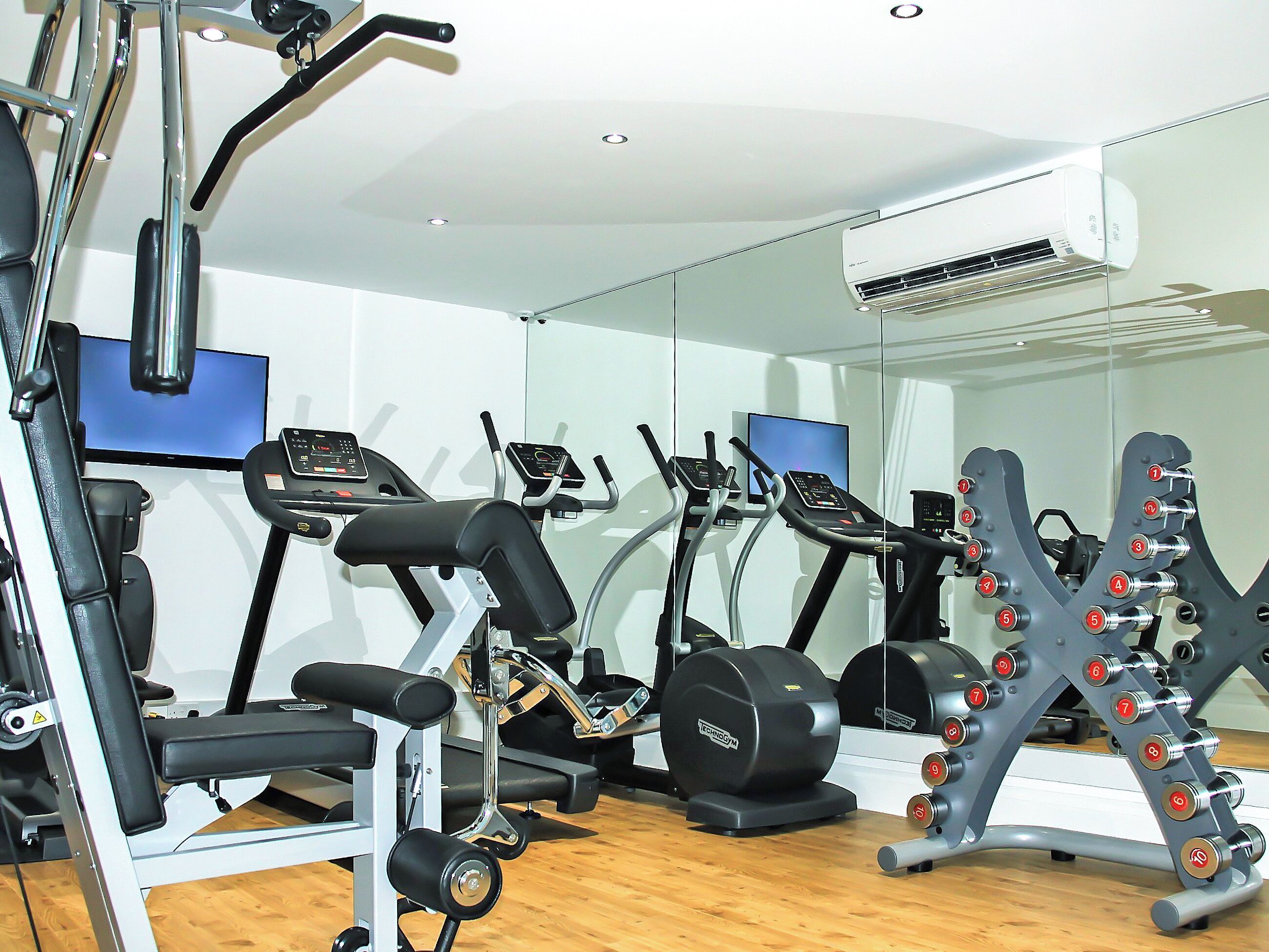 Ein Fitnessraum mit verschiedenen Trainingsgeräten, darunter Laufbänder, eine Gewichtbank und Kurzhanteln.